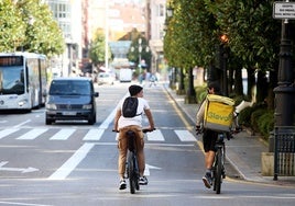 Unos jóvenes, en primer término, en bici por la calle Uría.