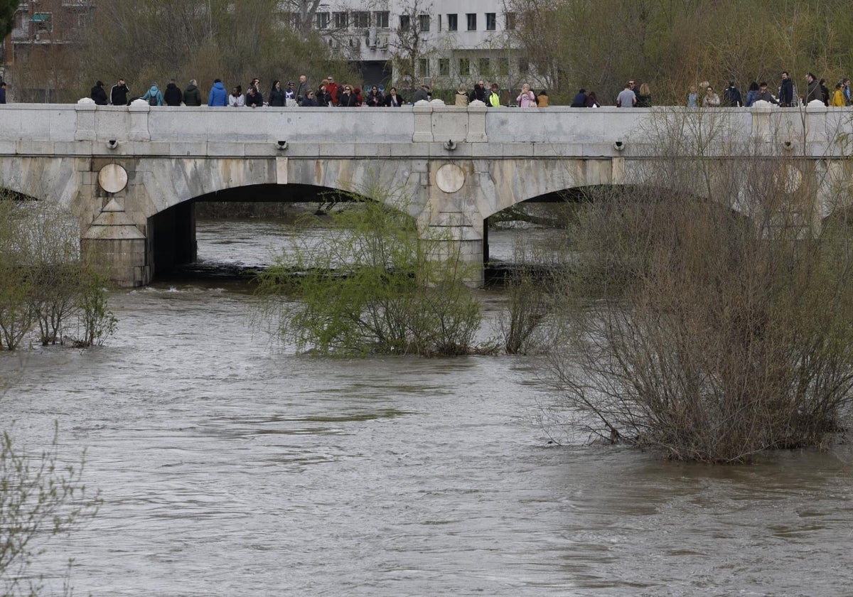 Varias personas observan el caudal del río Manzanares a su paso por Madrid.